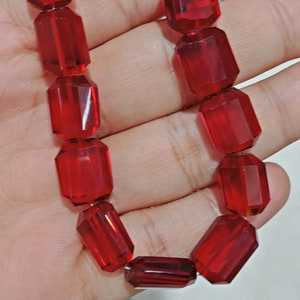 Puede incluir: Una hebra de cuentas de vidrio facetadas rojas. Las cuentas están enhebradas en un hilo transparente y están dispuestas en un patrón circular.