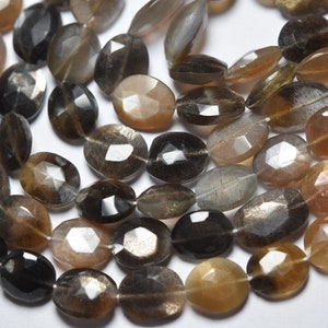 Può includere: Una collana di perle di pietra di sole sfaccettate in tonalità di marrone, oro e grigio. Le perle sono di forma ovale e hanno una qualità scintillante e iridescente.