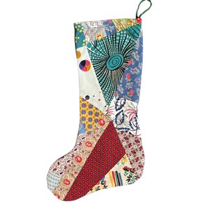 May include: A patchwork Christmas stocking with a green loop for hanging. The stocking is made of various fabric patterns, including floral, geometric, and abstract designs in red, blue, yellow, and white.