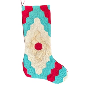 May include: A vintage Christmas stocking made of quilted fabric with a geometric pattern in red, white, and turquoise.
