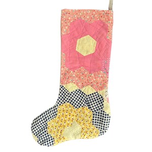 May include: A pink, yellow, and blue patchwork Christmas stocking with a hexagonal pattern.