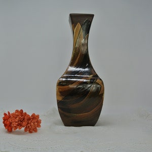 May include: A brown ceramic vase with a unique abstract design featuring swirling patterns in shades of brown, black, and gold. The vase has a narrow neck and a wide base.