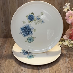 Peut inclure: Deux assiettes en céramique blanche avec un motif floral bleu et vert. Les assiettes sont rondes et empilées. Le motif comprend des formes géométriques et des motifs floraux.