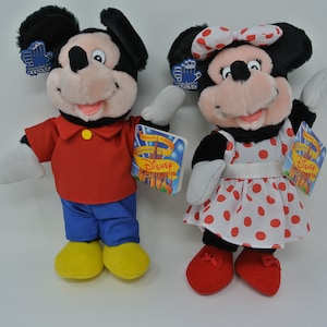 K&ouml;nnte beinhalten: Ein Paar Pl&uuml;schtiere von Mickey Mouse und Minnie Mouse. Mickey tr&auml;gt ein rotes Hemd, eine blaue Hose und gelbe Schuhe. Minnie tr&auml;gt ein wei&szlig;es Kleid mit roten Punkten, eine rote Schleife und rote Schuhe. Beide Spielzeuge haben Etiketten mit der Aufschrift "Disney".