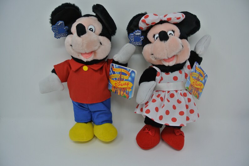 K&ouml;nnte beinhalten: Ein Paar Pl&uuml;schtiere von Mickey Mouse und Minnie Mouse. Mickey tr&auml;gt ein rotes Hemd, eine blaue Hose und gelbe Schuhe. Minnie tr&auml;gt ein wei&szlig;es Kleid mit roten Punkten, eine rote Schleife und rote Schuhe. Beide Spielzeuge haben Etiketten mit der Aufschrift "Disney".