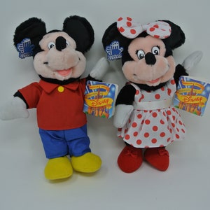 K&ouml;nnte beinhalten: Ein Paar Pl&uuml;schtiere von Mickey Mouse und Minnie Mouse. Mickey tr&auml;gt ein rotes Hemd, eine blaue Hose und gelbe Schuhe. Minnie tr&auml;gt ein rot-wei&szlig; gepunktetes Kleid mit einer wei&szlig;en Schleife. Beide Spielzeuge haben ein Disney-Etikett.