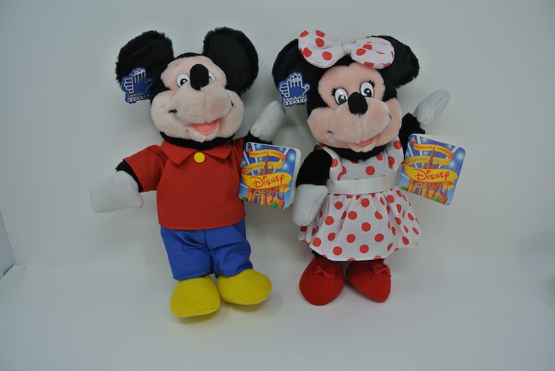K&ouml;nnte beinhalten: Ein Paar Pl&uuml;schtiere von Mickey Mouse und Minnie Mouse. Mickey tr&auml;gt ein rotes Hemd, eine blaue Hose und gelbe Schuhe. Minnie tr&auml;gt ein rot-wei&szlig; gepunktetes Kleid mit einer wei&szlig;en Schleife. Beide Spielzeuge haben ein Disney-Etikett.