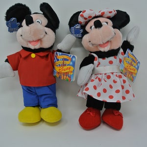 K&ouml;nnte beinhalten: Ein Paar Pl&uuml;schtiere von Mickey Mouse und Minnie Mouse. Mickey tr&auml;gt ein rotes Hemd, eine blaue Hose und gelbe Schuhe. Minnie tr&auml;gt ein rot-wei&szlig; gepunktetes Kleid mit einer wei&szlig;en Schleife und roten Schuhen. Beide Spielzeuge haben Etiketten mit der Aufschrift "Disney".