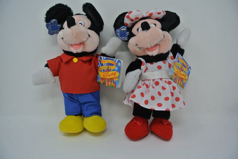 K&ouml;nnte beinhalten: Ein Paar Pl&uuml;schtiere von Mickey Mouse und Minnie Mouse. Mickey tr&auml;gt ein rotes Hemd, eine blaue Hose und gelbe Schuhe. Minnie tr&auml;gt ein rot-wei&szlig; gepunktetes Kleid mit einer wei&szlig;en Schleife und roten Schuhen. Beide Spielzeuge haben Etiketten mit der Aufschrift "Disney".