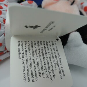 K&ouml;nnte beinhalten: Ein wei&szlig;es Etikett mit schwarzem Text beschreibt die Magie von Disney und wie diese Pl&uuml;schfiguren perfekt f&uuml;r die Spielzeit sind. Das Etikett ist an einem Pl&uuml;schtier von Mickey Mouse und Minnie Mouse befestigt.