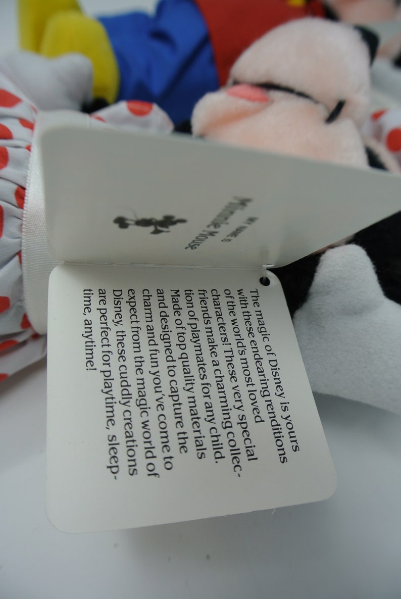 K&ouml;nnte beinhalten: Ein wei&szlig;es Etikett mit schwarzem Text beschreibt die Magie von Disney und wie diese Pl&uuml;schfiguren perfekt f&uuml;r die Spielzeit sind. Das Etikett ist an einem Pl&uuml;schtier von Mickey Mouse und Minnie Mouse befestigt.