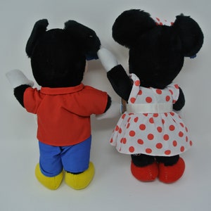 K&ouml;nnte beinhalten: Ein Paar Pl&uuml;schtiere, Mickey Mouse und Minnie Mouse, stehen R&uuml;cken an R&uuml;cken. Mickey tr&auml;gt ein rotes Hemd und eine blaue Hose, w&auml;hrend Minnie ein wei&szlig;es Kleid mit roten Punkten und einer roten Schleife tr&auml;gt.