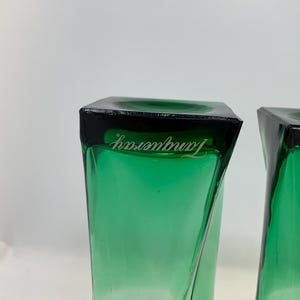Op de afbeelding: Twee groen getinte, vierkante glazen met een zwarte rand. Het woord "Tanqueray" is in het wit op de rand van elk glas gedrukt. De glazen hebben een gedraaid ontwerp.