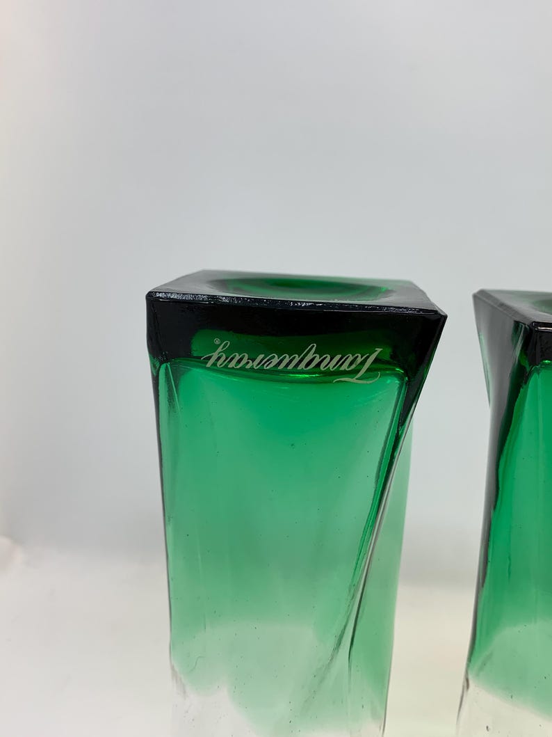 Op de afbeelding: Twee groen getinte, vierkante glazen met een zwarte rand. Het woord "Tanqueray" is in het wit op de rand van elk glas gedrukt. De glazen hebben een gedraaid ontwerp.
