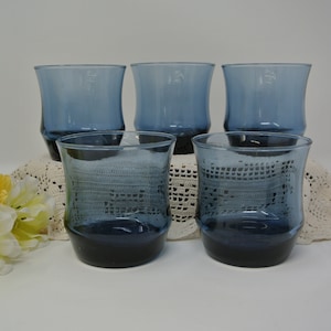 May include: Set of four blue glass tumblers with a rounded, flared shape. The glasses are clear and have a slight blue tint.
