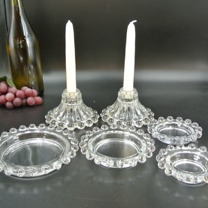 Könnte beinhalten: Set aus klaren Glaskerzenhaltern mit Perlenrand und passenden klaren Glasuntersetzern. Die Kerzenhalter haben ein geriffeltes Design und sind perfekt für Stumpenkerzen.
