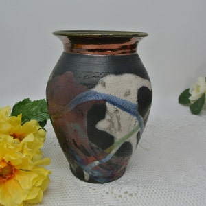 May include: A black ceramic vase with a copper-coloured rim and abstract painted designs in shades of white, blue, green, and red.