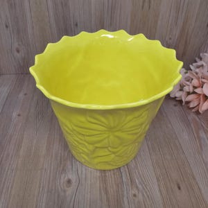 Puede incluir: Una maceta de cerámica amarilla con un borde festoneado y un diseño floral. La maceta está vacía y lista para una planta.