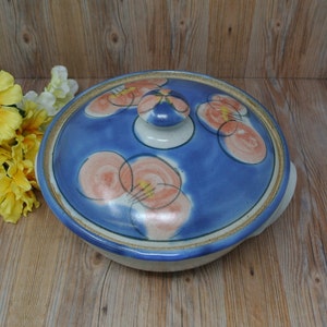 Puede incluir: Un plato de servir de cerámica azul y blanco con tapa. La tapa tiene un diseño floral con flores rosas y naranjas. El plato tiene un borde marrón.