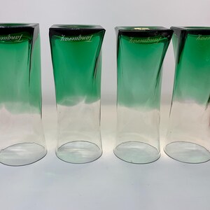 Op de afbeelding: Vier heldere, groen getinte glazen bekers met een vierkante bovenkant en gebogen zijkanten. De bovenste rand is zwart en het woord "Tanqueray" is in het wit gedrukt. De glazen hebben een gradi&euml;nteffect, van groen naar helder.