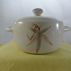 Puede incluir: Plato de cerámica blanco para hornear con tapa y dos asas. El plato tiene un diseño estilizado de hojas marrones y beige.