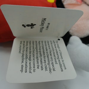 K&ouml;nnte beinhalten: Ein wei&szlig;es Etikett mit schwarzem Text, der "MY NAME IS Mickey Mouse" lautet. Das Etikett hat eine schwarze Silhouette von Mickey Mouse in der oberen linken Ecke. Der Text auf dem Etikett lautet: "Die Magie von Disney geh&ouml;rt dir mit diesen liebenswerten Nachbildungen der beliebtesten Figuren der Welt! Diese ganz besonderen Freunde bilden eine charmante Sammlung von Spielkameraden f&uuml;r jedes Kind. Hergestellt aus hochwertigen Materialien und so konzipiert, dass sie den Charme und den Spa&szlig; einfangen, den du aus der magischen Welt von Disney kennst, sind diese kuscheligen Kreationen perfekt f&uuml;r Spielzeit, Schlafenszeit, jederzeit!"