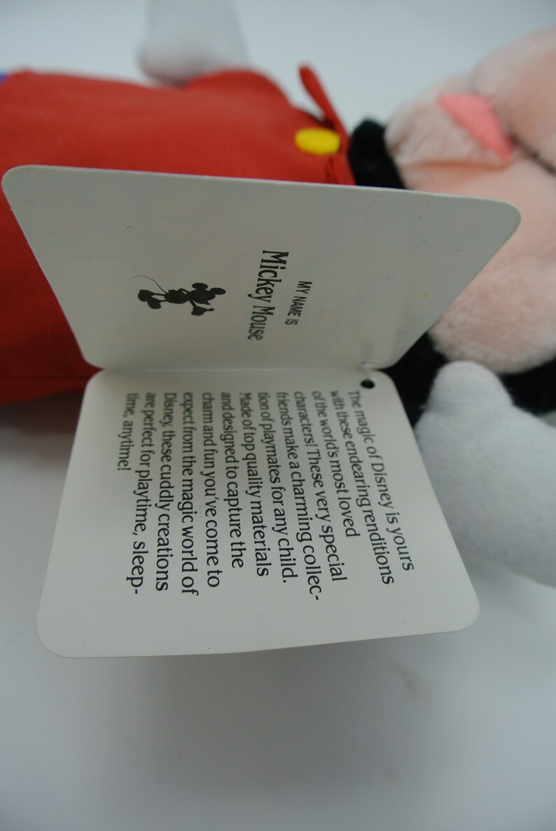 K&ouml;nnte beinhalten: Ein wei&szlig;es Etikett mit schwarzem Text, der "MY NAME IS Mickey Mouse" lautet. Das Etikett hat eine schwarze Silhouette von Mickey Mouse in der oberen linken Ecke. Der Text auf dem Etikett lautet: "Die Magie von Disney geh&ouml;rt dir mit diesen liebenswerten Nachbildungen der beliebtesten Figuren der Welt! Diese ganz besonderen Freunde bilden eine charmante Sammlung von Spielkameraden f&uuml;r jedes Kind. Hergestellt aus hochwertigen Materialien und so konzipiert, dass sie den Charme und den Spa&szlig; einfangen, den du aus der magischen Welt von Disney kennst, sind diese kuscheligen Kreationen perfekt f&uuml;r Spielzeit, Schlafenszeit, jederzeit!"