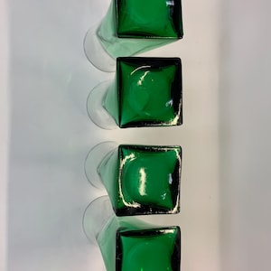 Op de afbeelding: Vier groene glazen vazen met vierkante bovenkanten en lange, heldere stelen zijn verticaal gerangschikt. De vazen hebben een glanzende afwerking en de groene kleur is levendig. De heldere stelen cre&euml;ren een contrast.