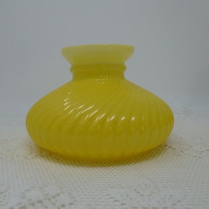 May include: A yellow glass lampshade with a swirl design. The lampshade is made of opaque glass and has a white top.