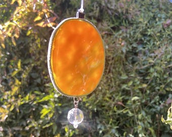 May include: A round, orange stained glass sun catcher with a clear crystal hanging from the bottom.