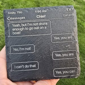May include: A dark gray slate coaster with a text message conversation etched on its surface. The messages include phrases like "Yeah, but I'm not drunk enough to go out on a boat!" and "Yes, you are."