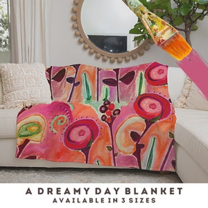 May include: A pink, orange, and green floral patterned throw blanket with the text "A Dreamy Day Blanket Available in 3 Sizes".