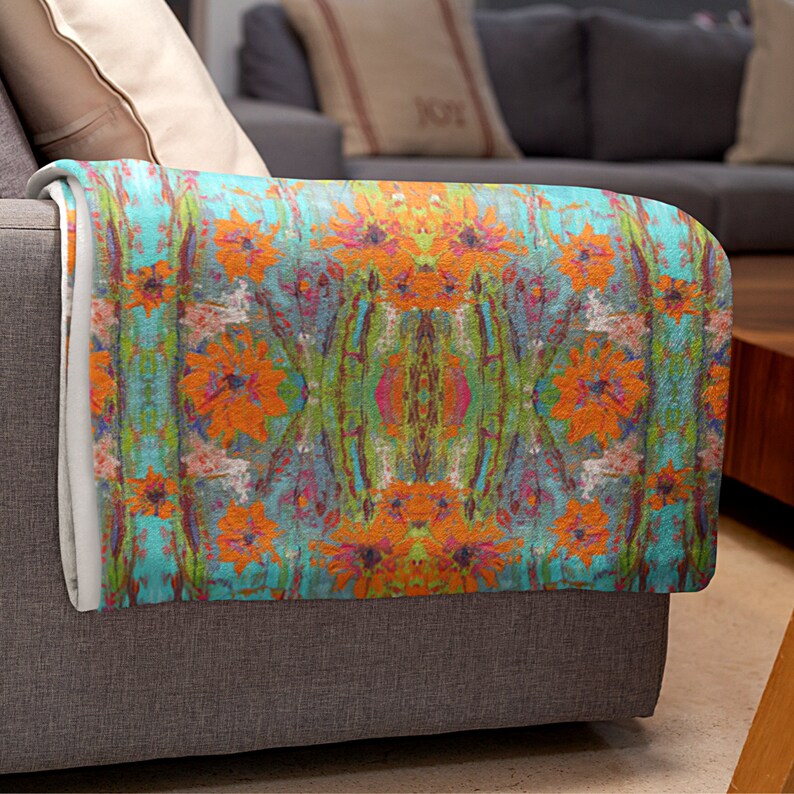 May include: A teal, orange, and green patterned throw blanket with a floral design. The blanket is folded and draped over a gray couch.
