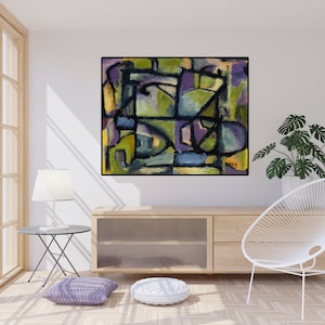 May include: Abstract painting with geometric shapes in shades of green, purple, blue, and yellow. The painting is framed in black and hangs on a white wall in a living room setting.
