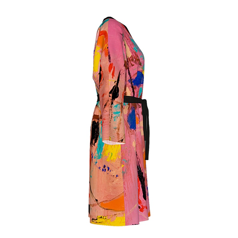Op de afbeelding: Een roze en zwarte lange jurk met lange mouwen met een abstract verfspattenontwerp in verschillende kleuren, waaronder geel, blauw en oranje. De jurk heeft een zwarte riem.