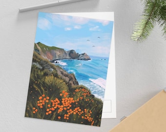 May include: A postcard featuring a painting of a coastal scene with a rocky cliff, orange flowers, and a blue ocean with white waves. The sky is blue with white clouds and there are birds flying in the sky.