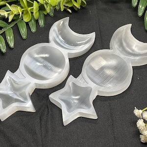May include: White selenite crystal dish with three compartments shaped like a crescent moon, a circle, and a star. The dish is made of polished selenite and has a smooth, white surface.