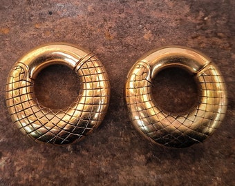 Puede incluir: Dos medidores de oreja de metal de color dorado con un diseño texturizado en forma de serpiente. Los medidores son circulares y tienen un centro hueco.