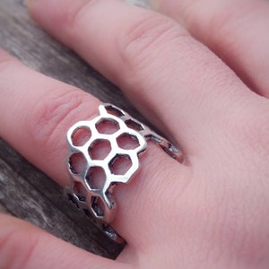 Può includere: Un anello d'argento con un design a nido d'ape. L'anello è indossato su un dito.
