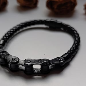 以下が含まれることがあります： 自転車のチェーンデザインが特徴の黒いブレスレット。ブレスレットは編み革バンドとチェーンリンククラスプを備えています。ブレスレットは濃いマットブラック色です。ユニークなアクセサリーです。