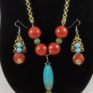 May include: A necklace and earring set featuring red, turquoise, and green beads. The necklace has a gold chain with large red and turquoise beads. The earrings have a similar design with smaller beads and gold wire accents. The jewelry is displayed against a black background.