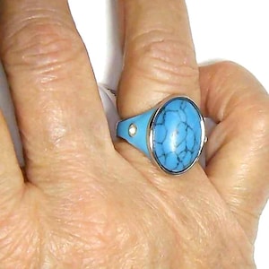 May include: A silver ring with a blue oval turquoise stone set in a silver band. The ring has two small silver dots on the band.