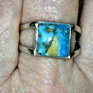 May include: A silver ring with a rectangular turquoise stone. The stone has a mix of blue, green, and brown colors. The ring has a simple, modern design.