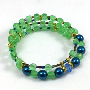 May include: A beaded bracelet featuring green and blue beads. The bracelet has multiple strands of light green, translucent beads, interspersed with gold-colored accents and dark blue, round beads. The design is a spiral wrap style.