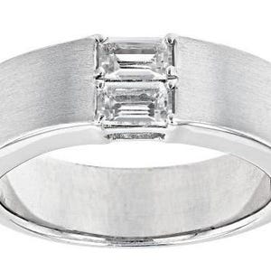 May include: A silver ring with a brushed finish and two rectangular, clear gemstones set in the center. The ring has a wide band and a polished interior.