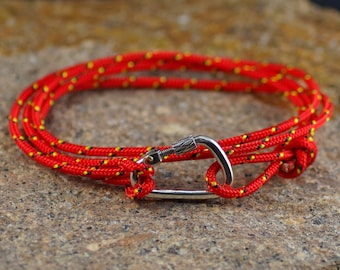 May include: A red and yellow rope bracelet with a silver carabiner clasp.