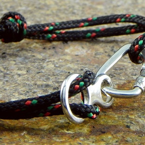 May include: A black rope bracelet with red and green accents, featuring a silver carabiner clasp.