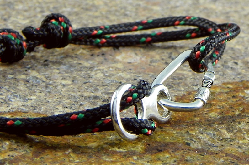 May include: A black rope bracelet with red and green accents, featuring a silver carabiner clasp.