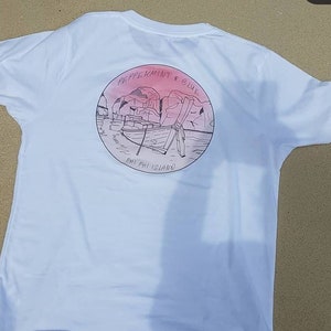 May include: White t-shirt with a circular graphic on the back. The graphic features a pink and blue sunset over a boat with the text "Peppermint & Blue" and "Phi Phi Island".