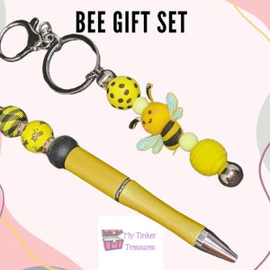 Op de afbeelding: Een bij-thema cadeauset met een gele pen met zwarte en gele kralen en een sleutelhanger met een gele bij-hanger en gele en zwarte kralen. De tekst "BEE GIFT SET" staat bovenaan de afbeelding.